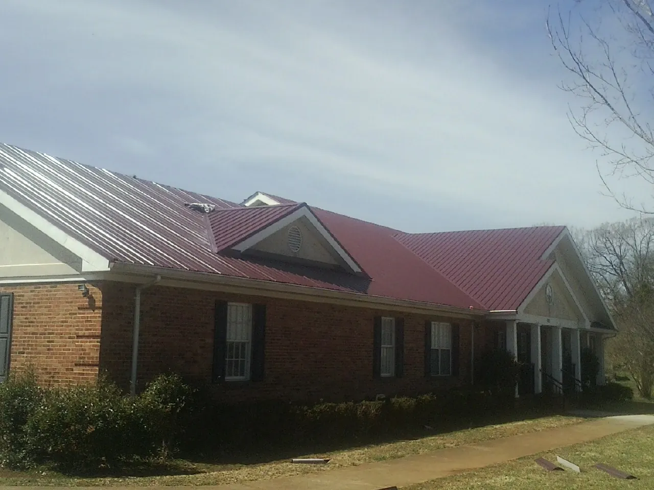 Red metal roof with gabled entries on a long brick building, from a Hail Damage Roof Repair job in New Philadelphia
