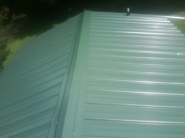 New green metal panels meeting at the ridge of a roof — Flat Roof Repair work by our crew in New Philadelphia