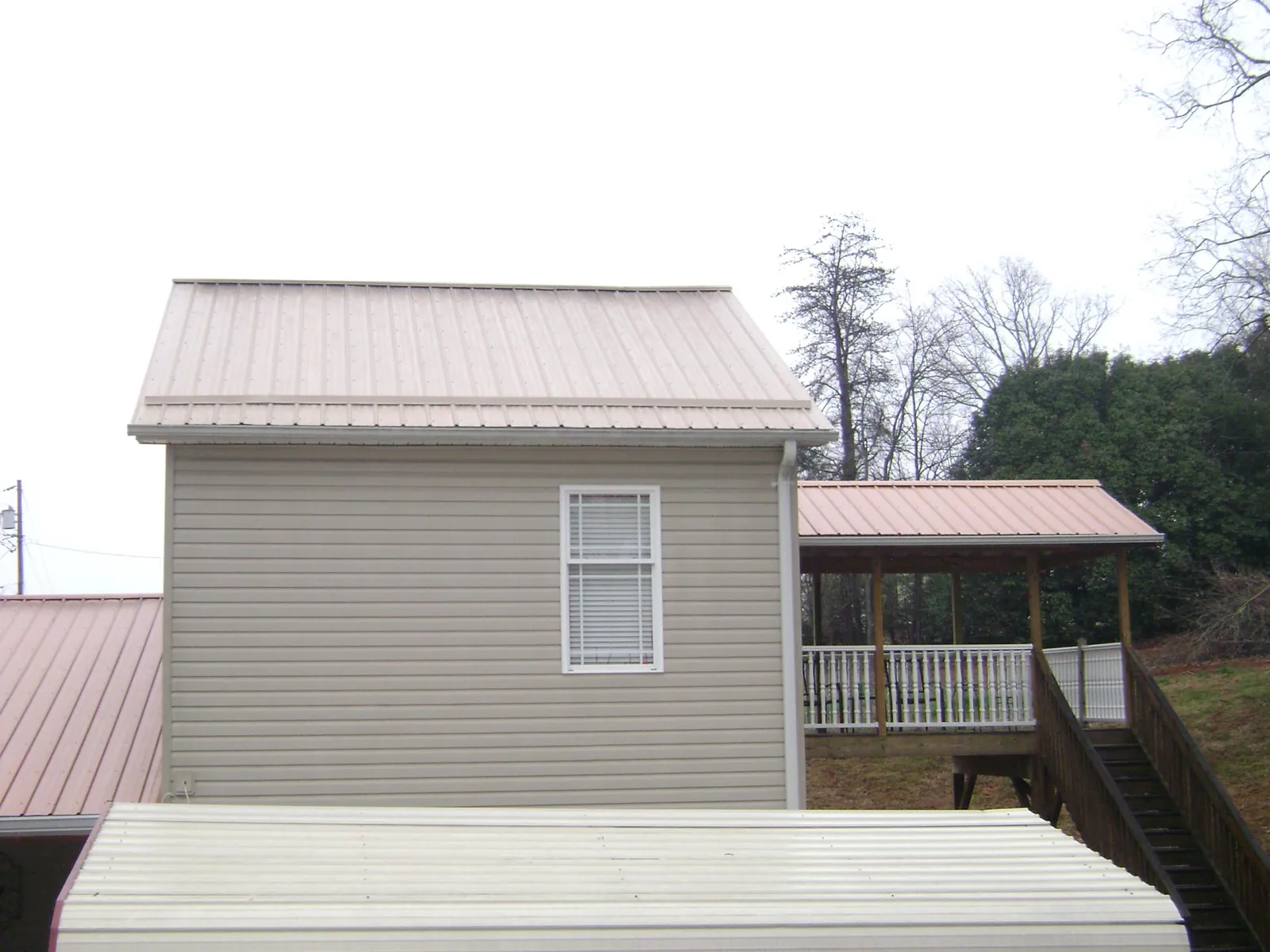 Tan metal roofs on a two story addition and attached porch, from a Roof Replacement job in New Philadelphia
